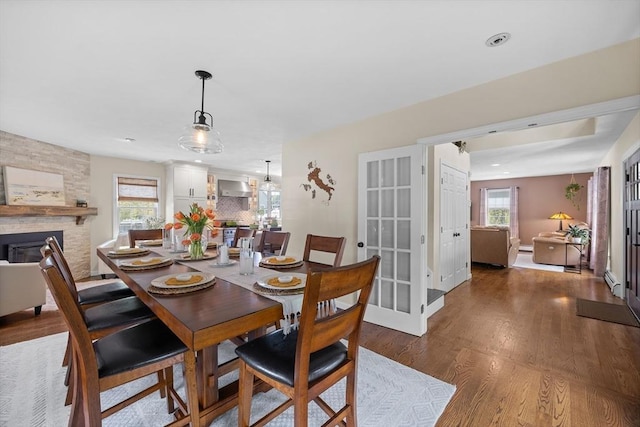dining room with wood finished floors, plenty of natural light, a stone fireplace, baseboards, and recessed lighting