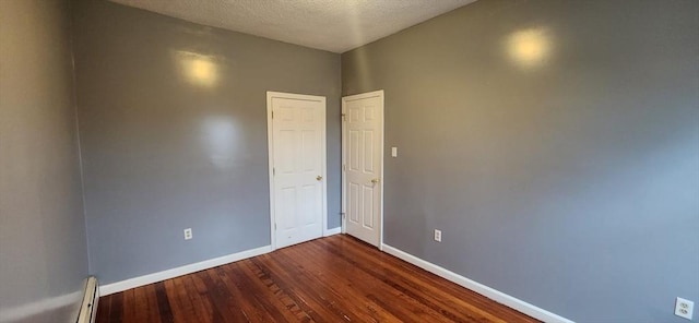 spare room featuring a textured ceiling, baseboard heating, dark wood finished floors, and baseboards