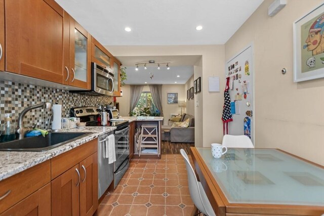 kitchen with appliances with stainless steel finishes, a sink, tasteful backsplash, glass insert cabinets, and brown cabinetry