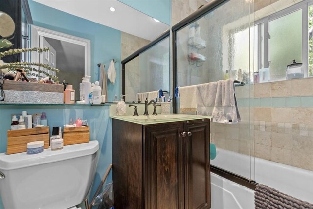 bathroom featuring toilet, vanity, and combined bath / shower with glass door