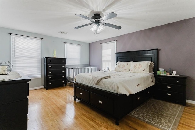 bedroom with light wood-style floors, baseboards, visible vents, and a ceiling fan