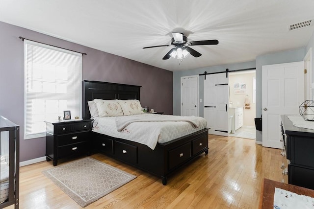 bedroom with visible vents, light wood-style flooring, a barn door, ceiling fan, and baseboards