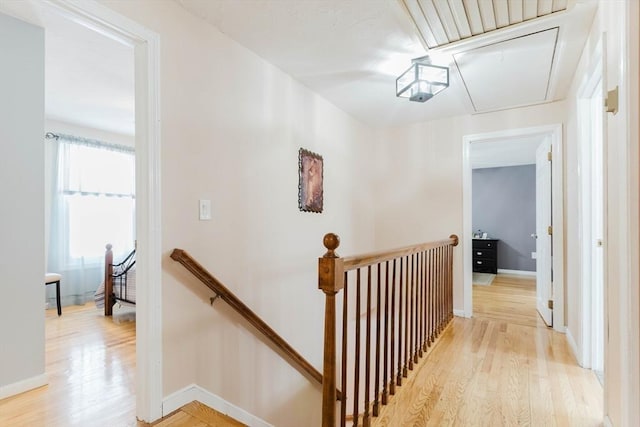 hall featuring light wood-style floors, attic access, baseboards, and an upstairs landing