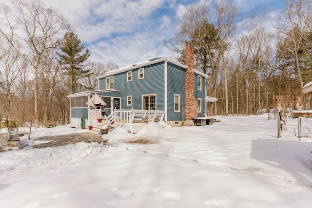 snow covered property featuring a sunroom and a chimney