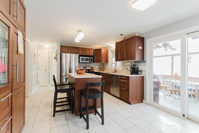 kitchen with a kitchen island, a sink, light countertops, appliances with stainless steel finishes, and a kitchen bar