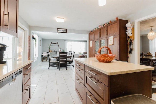 kitchen with light tile patterned floors, a kitchen island, light countertops, brown cabinets, and dishwasher