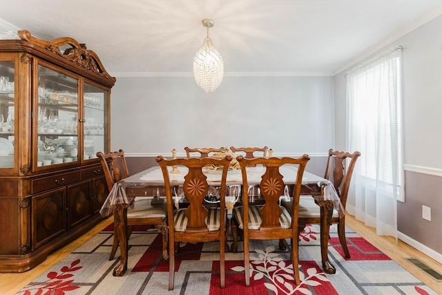 dining area featuring light wood finished floors, baseboards, visible vents, an inviting chandelier, and crown molding