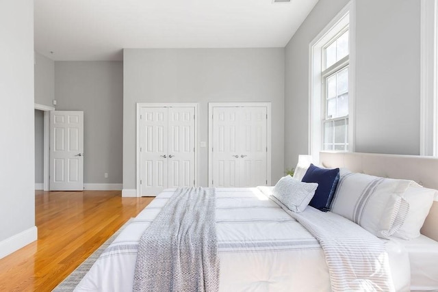 bedroom featuring two closets, wood finished floors, and baseboards