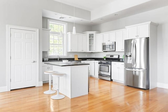 kitchen with appliances with stainless steel finishes, light wood-style flooring, white cabinets, a kitchen island, and hanging light fixtures