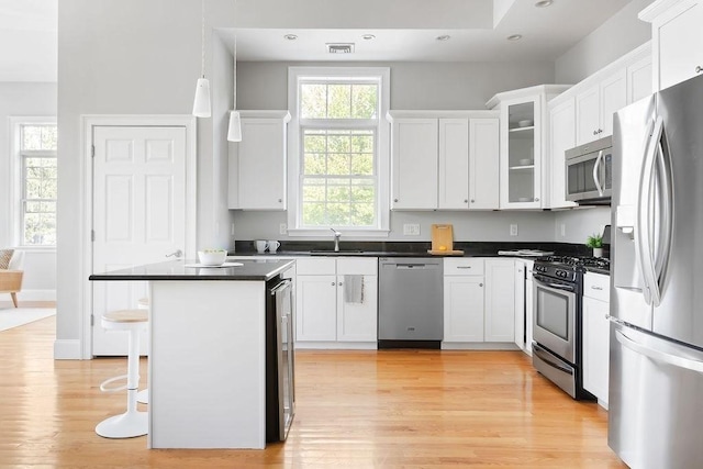 kitchen with stainless steel appliances, a sink, white cabinetry, light wood finished floors, and a breakfast bar area