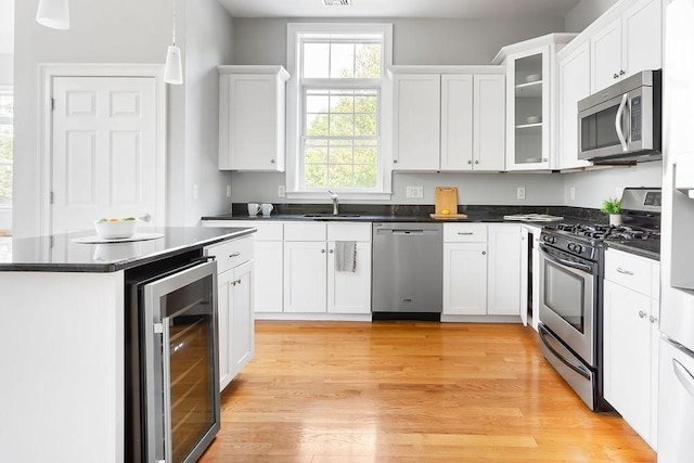kitchen featuring stainless steel appliances, wine cooler, a sink, dark countertops, and white cabinets