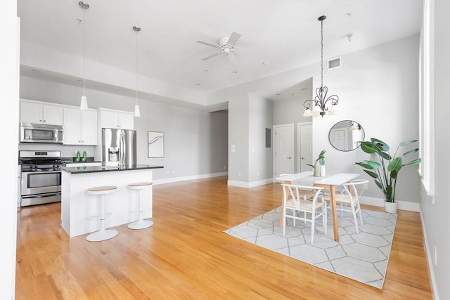dining room with light wood-style flooring, ceiling fan, baseboards, a chandelier, and a high ceiling
