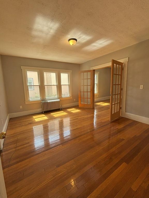 723 White St, Springfield, MA 01108 - spare room featuring radiator heating unit, baseboards, wood finished floors, and a textured ceiling