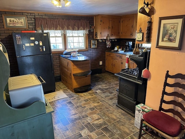 kitchen with black refrigerator, brick wall, and stove