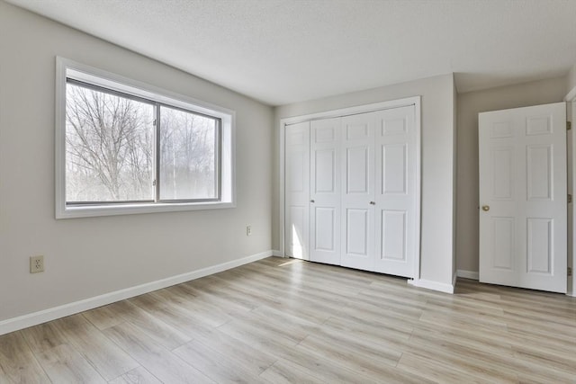 unfurnished bedroom featuring light wood-style floors, baseboards, and a closet