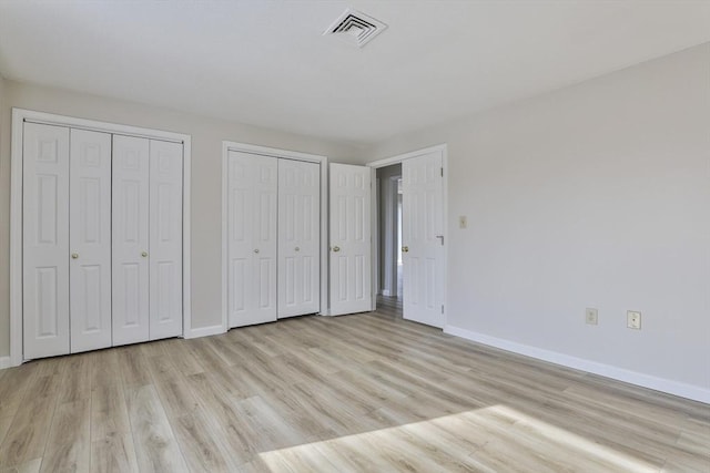 unfurnished bedroom featuring visible vents, multiple closets, baseboards, and light wood-style flooring