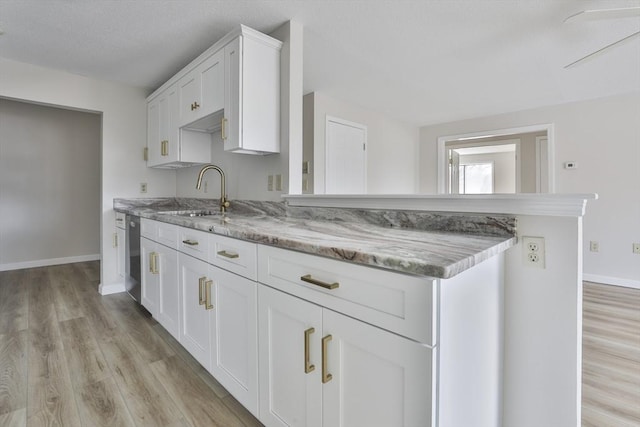 kitchen with light wood-style flooring, a sink, a peninsula, white cabinets, and baseboards