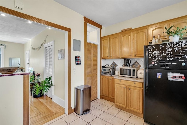kitchen featuring stainless steel microwave, tasteful backsplash, freestanding refrigerator, light tile patterned flooring, and light countertops