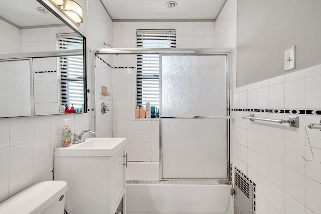 full bath with tile walls, vanity, combined bath / shower with glass door, and a wealth of natural light