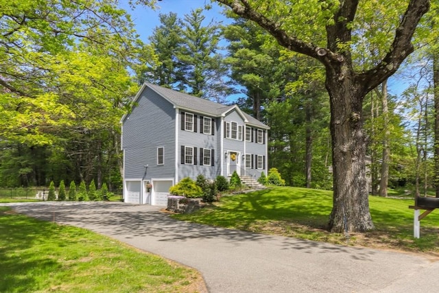 colonial house with a garage, asphalt driveway, and a front lawn