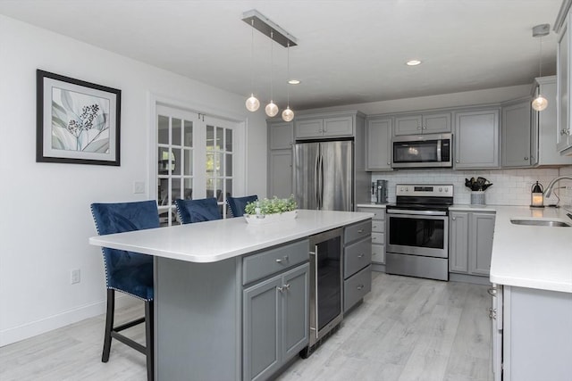 kitchen featuring stainless steel appliances, gray cabinets, beverage cooler, a sink, and a breakfast bar area