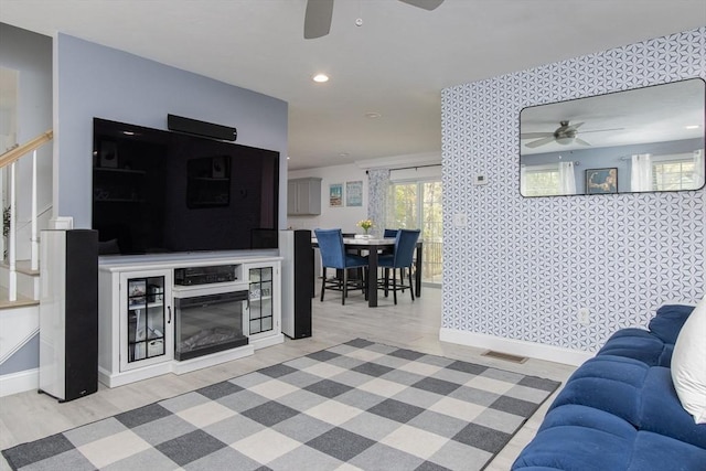 living area with ceiling fan, wallpapered walls, baseboards, wood finished floors, and stairway