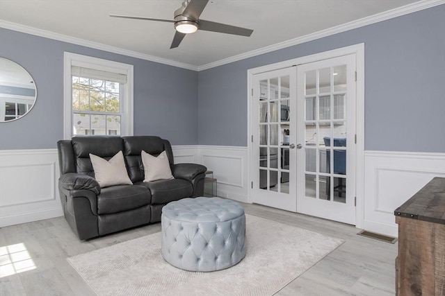 living area featuring french doors, wood finished floors, ceiling fan, wainscoting, and ornamental molding
