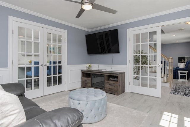 living room with french doors, wood finished floors, ceiling fan, crown molding, and wainscoting