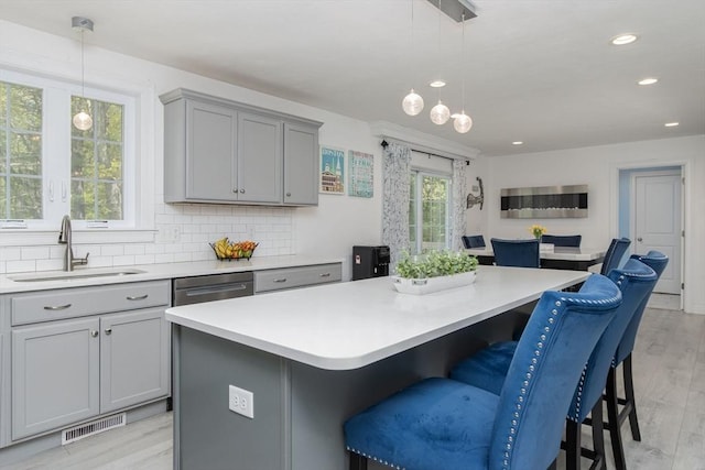 kitchen featuring gray cabinetry, a sink, a kitchen island, backsplash, and light countertops