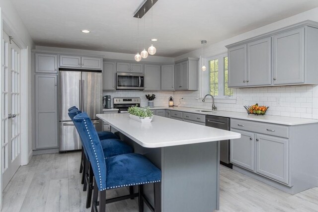 kitchen featuring appliances with stainless steel finishes, gray cabinetry, a sink, light wood-type flooring, and a kitchen breakfast bar