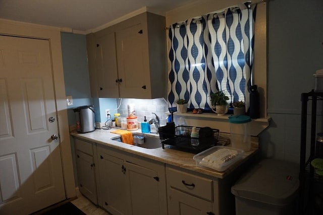 kitchen with white cabinetry, light countertops, a sink, and ornamental molding