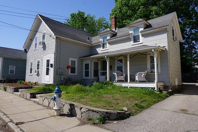 view of front of home with a porch, a chimney, a shingled roof, and cooling unit