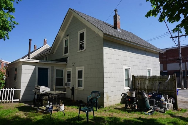 rear view of house with a chimney and roof with shingles