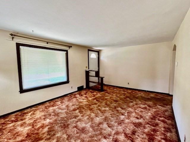 carpeted empty room featuring arched walkways and baseboards