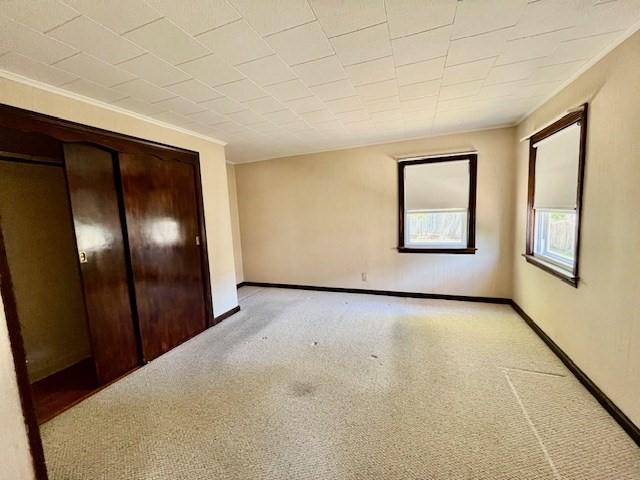 unfurnished bedroom with baseboards, a closet, light colored carpet, and crown molding