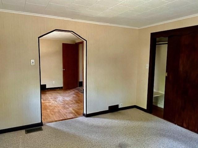 carpeted spare room with arched walkways, crown molding, and baseboards