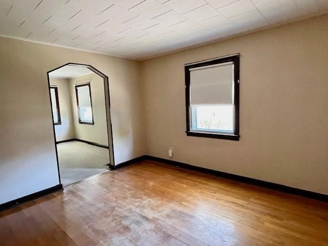 spare room with wood finished floors, baseboards, and arched walkways