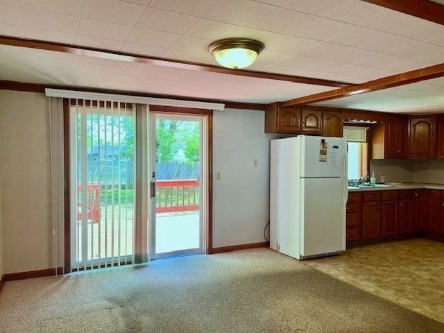 kitchen featuring freestanding refrigerator, light colored carpet, light countertops, and baseboards