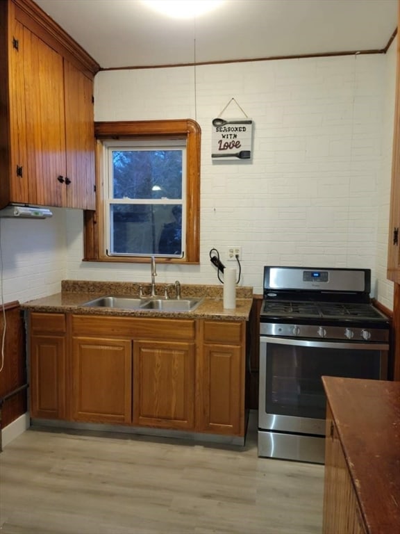 kitchen with dark stone countertops, stainless steel gas range oven, light hardwood / wood-style flooring, and sink