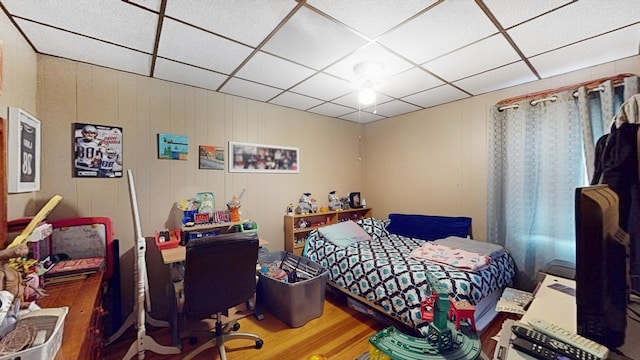 bedroom with a drop ceiling, wood walls, and hardwood / wood-style floors