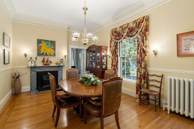 dining room featuring light hardwood / wood-style floors, a chandelier, radiator, a fireplace, and ornamental molding