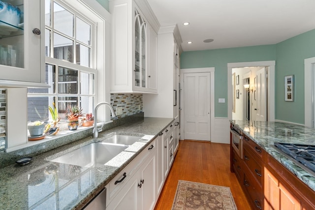 kitchen with light stone counters, decorative backsplash, wood-type flooring, white cabinets, and sink