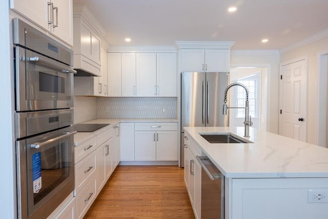 kitchen with stainless steel appliances, white cabinetry, a sink, and light stone countertops