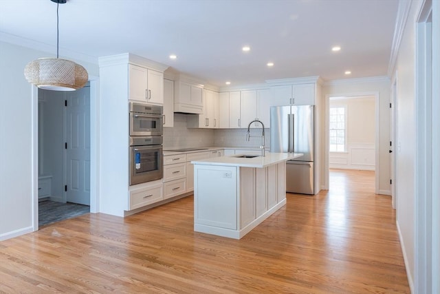 kitchen with hanging light fixtures, a kitchen island with sink, stainless steel appliances, light countertops, and white cabinetry