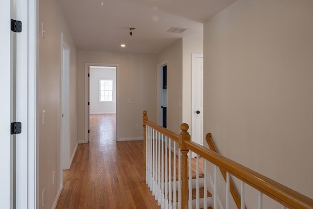 hall with light wood finished floors, baseboards, visible vents, and an upstairs landing