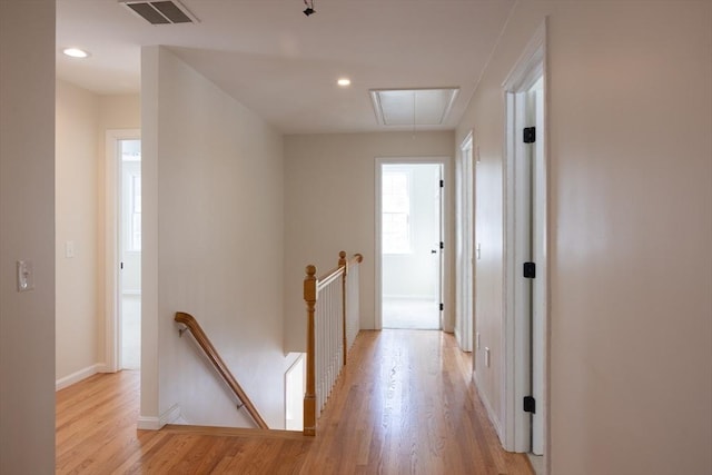 corridor featuring light wood finished floors, attic access, visible vents, and an upstairs landing