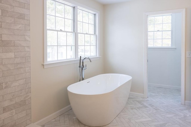 full bath featuring plenty of natural light, a soaking tub, and baseboards