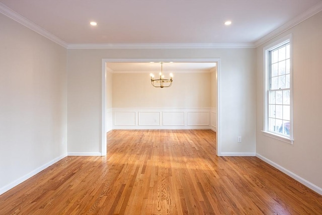 spare room featuring a decorative wall, a wainscoted wall, ornamental molding, light wood-type flooring, and an inviting chandelier