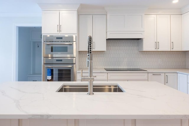 kitchen featuring white cabinets, light stone counters, black electric cooktop, double oven, and backsplash