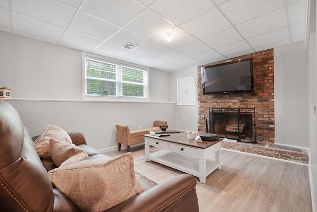living area featuring light wood finished floors, a paneled ceiling, baseboards, and a brick fireplace